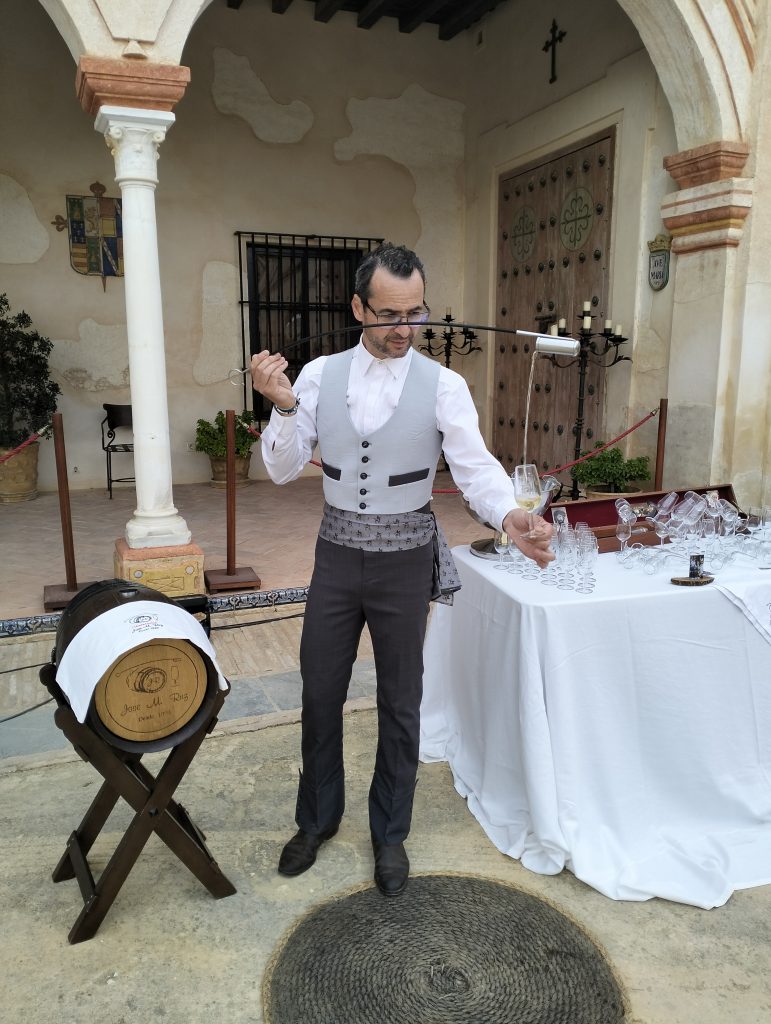 José Manuel Ruz venenciando junto a un barril de vino en un evento en Montilla
